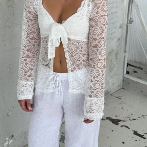 Vit spetsblus med knytning - Säljer en elegant vit spetsblus med långärmad design och knytning framtill. Perfekt för en stilfull look med sitt vackra blommönster och transparenta material.