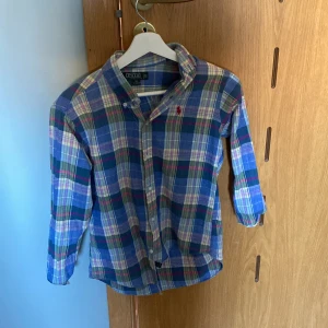Rutig skjorta från Polo Ralph Lauren - Säljer en snygg rutig skjorta från Polo Ralph Lauren i blått, grönt och rosa. Skjortan har långa ärmar och knappar framtill. Den är broderad med det klassiska Polo Ralph Lauren-märket på bröstet. Perfekt för en stilren look!
