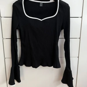 Svart topp med vit kant - Snygg svart  topp från Shein med vit kant runt halsringningen och ärmar.Toppen har långa ärmar och en unik fyrkantig hals. Perfekt för en stilren look.