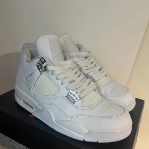Air Jordan retro 4s pure money  - Snygga vita Nike Air Jordans med klassisk design och silverdetaljer. Skorna har snörning och en rund tå, vilket ger en stilren look. Perfekta för dig som vill ha en stilren och sportig stil.