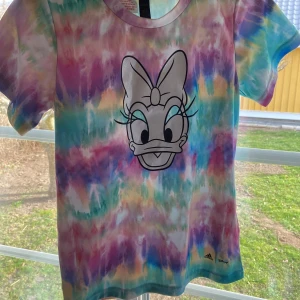 Färgglad t-shirt med Daisy-motiv från Adidas - Säljer en superfin t-shirt från Adidas med ett färgglatt tie-dye mönster och en stor Daisy-anka på framsidan. Perfekt för att liva upp garderoben! 💜
