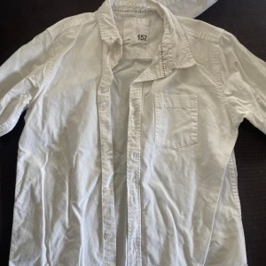 Vit skjorta från 157 barn  - Säljer en klassisk vit skjorta från 157. Skjortan har en bröstficka och knappar framtill. Perfekt för en stilren look.