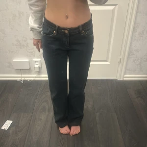 Mörkblå jeans med raka ben - Snygga mörkblå jeans med raka ben och låg midja. Klassisk design med knappar och dragkedja framtill. Perfekta för en avslappnad stil.