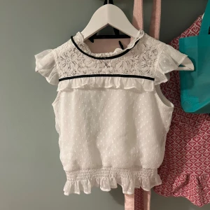 Vit blus med spetsdetaljer - Söt vit blus med spetsdetaljer och volanger. Blusen har korta ärmar och en fin spetskrage. Perfekt för en somrig look.