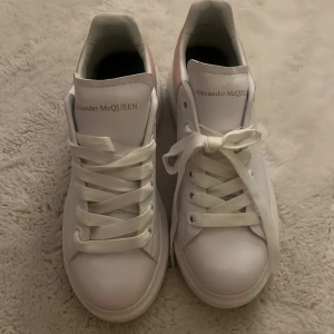 Vita sneakers från Alexander McQueen - Snygga vita sneakers från Alexander McQueen med rosa detaljer på hälen. Skorna har klassisk snörning och en stilren design som passar perfekt för en trendig look. Dom är tyvärr för stora för mig, så kommer inte till användning. Ordinarie pris: 5149