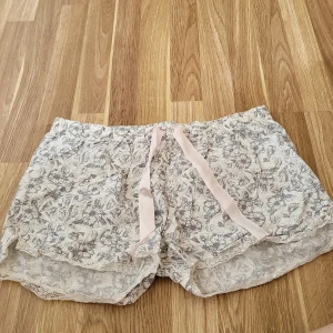 Pyjamasshorts - Säljer ett par bekväma blommiga shorts i 100% bomull. De har ett fint mönster i grått och vitt samt ett rosa knytband i midjan. Perfekta för varma sommardagar!