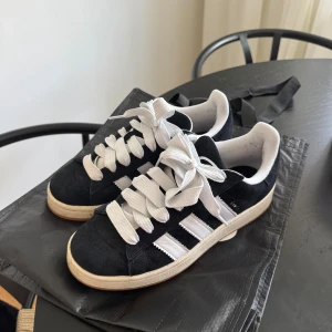 Svarta Adidas Campus sneakers - Snygga svarta Adidas Campus sneakers med vita ränder och snörning. Super sköna skor men säljer då dom inte kommer till användning, endast används ca 3 gånger.