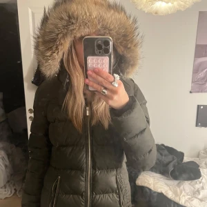 Dunjacka med pälsdetaljer - (ÄKTA) Säljer en varm och stilren mörkgrön dunjacka från snoot med en stor huva kantad med päls. Ny pris är 7000 därav högt pris🩷