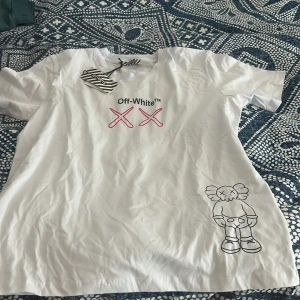 Vit t-shirt från Off-White - Säljer en vit t-shirt från Off-White med rosa XX-motiv och en tecknad figur på framsidan. Baksidan har ett stort tryck med texten 'As Soon As Possible' och '99'. Perfekt för dig som gillar streetwear!