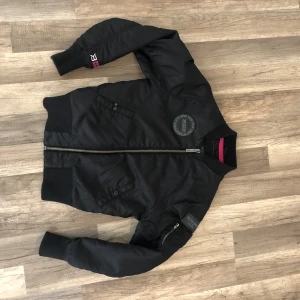 Svart bomberjacka från Better Bodies - Snygg svart bomberjacka från Better Bodies med quiltad insida och dragkedja framtill. Jackan har ribbade muddar och en diskret logga på bröstet. Perfekt för en cool och avslappnad stil.