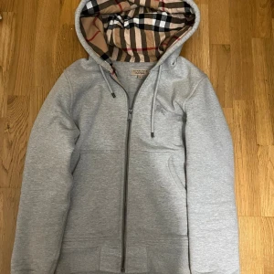 Burberry kofta  - Säljer två hoodies, en grå och en svart, båda med dragkedja och rutigt foder i huvan. De har en broderad logga på bröstet och är perfekta för en avslappnad stil. Passar bra till både höst och vår. Den svarta koftan har en liten del av dragkedjan som är borta men man märker nästan inte ens av den men annars är allt som det ska om ni undrar nåt så är det bara att skriva 😁