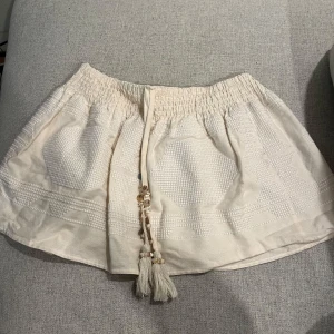 Beige kjol med knytband - Charmig beige kjol med elastisk midja och dekorativa knytband med tofsar. Kjolen har en subtil textur och är perfekt för varma dagar. Midjan är om sydd så att den är lågmidjad. Pris kan diskuteras och jag är villig till att sänka priset!!