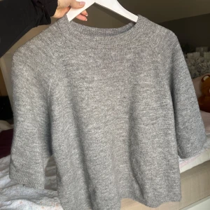 Grå stickad tröja från 157 - Säljer en stilren grå stickad tröja från 157. Tröjan har en klassisk rund hals och trekvartsärmar, perfekt för lager på lager under kyligare dagar. Den är mjuk och bekväm, idealisk för både vardag och avslappnade tillfällen. Passar perfekt till jeans eller kjol!