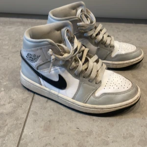 Nike Air Jordans i vitt och grått - Säljer ett par klassiska Nike Air Jordans Mid i vitt och grått.. Stl 36 (innermått ca 23  cm). Gott skick.