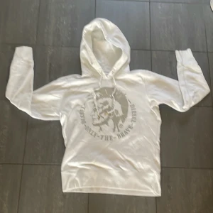 Vit hoodie från Diesel - Säljer en vit hoodie från Diesel med trycket 'Only The Brave' och en cool grafisk design på framsidan. Tröjan har långa ärmar och en klassisk huva. Perfekt för en avslappnad stil.