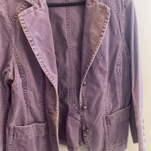 Lila kavaj från Lindex - Säljer en snygg lila kavaj från Lindex med knappar framtill och två stora fickor. Kavajen har långa ärmar och en klassisk krage. Perfekt för att ge din outfit en färgklick!