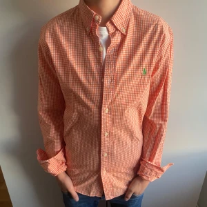 Ralph Lauren skjorta - Ralph Lauren-skjorta i orange och vitt småmönstrat rutmönster med grön logga. Klassisk modell i nyskick, passar alla tillfällen. Storleken är S slimfit.