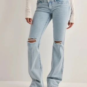 Ljusblå bootcut jeans med broderade fickor - Snygga ljusblå bootcut jeans med slitna detaljer på knäna och coola broderade fickor baktill. Perfekta för en avslappnad stil med en touch av edge.