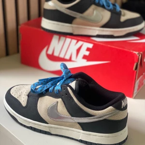 Nike Dunk Low Light Bone/Metallic Silver  - Nike Dunk Low WMNS “Light Bone / Metallic Silver” Storlek: US 7.5 / EU 38.5 (24.5 cm) Sparsamt, knappt använda – fint skick! Kommer med originalkartong. Blå skosnören (original kan skickas med vid önskemål).  Pris: 1 100 kr  