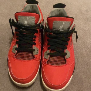 Röda Nike Air Jordans - Snygga röda Nike Air Jordans med svarta och grå detaljer. Skorna har en klassisk snörning och en ikonisk Jumpman-logga på hälen. Perfekta för dig som vill ha en stilren och sportig look.