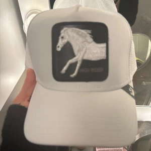 The farm keps - Snygg vit keps med ett broderat hästmotiv på framsidan. Kepsen har en klassisk design med justerbar passform och nätpaneler på sidorna för extra ventilation. Perfekt för en avslappnad stil.
