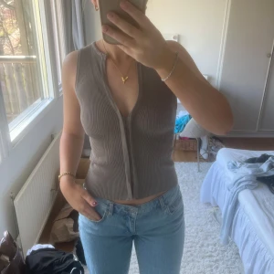 Beige ribbad linnetopp från Zara - Säljer en snygg beige ribbad linnetopp från Zara. Toppen är ärmlös och har en dragkedja framtill som ger en cool look. Perfekt för varma dagar eller som ett lager under en jacka.