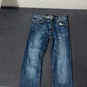Blå jeans från SMOG - Säljer ett par klassiska blå jeans från SMOG. De har en normal passform med fem fickor och en dragkedja. Perfekta för en avslappnad stil. 