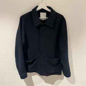 Mörkblå jacka från Lindbergh - Säljer en stilren mörkblå jacka från Lindbergh. Jackan har en klassisk krage och knäppning framtill med fem knappar. Den har två praktiska fickor framtill och är långärmad. Perfekt för en stilren look.