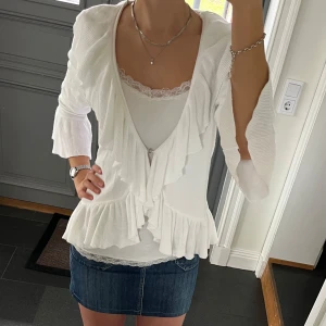 Vit stickad kofta med volanger  - Trekvartsärmad vit stickad kofta i storlek M från Lindex. Skulle säga att den även passar S. Fint skick. Använd gärna köp nu!