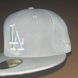 Grå keps från New Era - Snygg grå keps från New Era med LA-logga framtill och 1988 World Series-brodyr på sidan. Kepsen är en del av 59FIFTY-serien och har en klassisk passform. Perfekt för att ge din outfit en sportig touch.