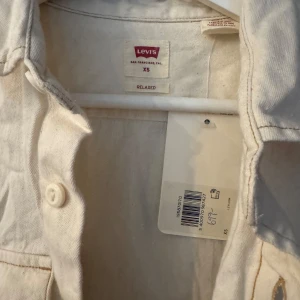 Beige skjorta från Levi's - Säljer en beige skjorta från Levi's i storlek XS. Skjortan har en relaxed passform med långa ärmar och knappar framtill. Perfekt för en avslappnad stil.