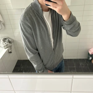 Grå kofta med dragkedja - Säljer en stilren grå kofta med dragkedja framtill. Perfekt för lager-på-lager och passar till många olika outfits. Koftan har långa ärmar och en bekväm passform.