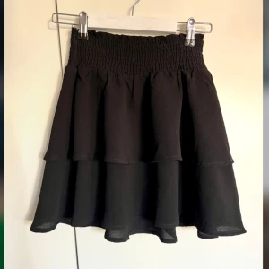 Svart volangkjol - Snygg svart kortkjol med volanger. Insydd lite grann i midjan.