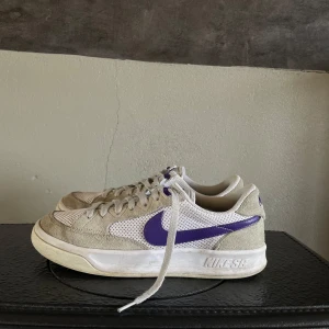 Nike SB sneakers med lila detaljer - Säljer ett par Nike SB adversary sneakers i beige och vitt med lila swoosh och detaljer. Skorna har snörning och en klassisk design med en bekväm passform. Perfekta för en avslappnad stil. Gillar dessa skor verkligen men tyvärr har de blivit för små. Storlek 42. Priset kan diskuteras vid snabb affär!