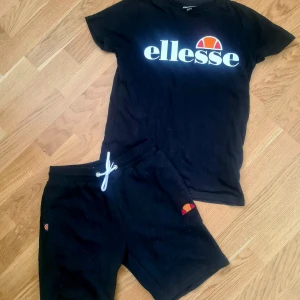 Svart t-shirt från Ellesse - Säljer en svart t-shirt från Ellesse med deras ikoniska logga i vitt och orange på bröstet. Perfekt för en sportig och avslappnad stil. Passar ungdomar i storlek 152-158.....Matchande shorts till,,båda som nytt......Djur och rökfritt...250kr för båda ihop