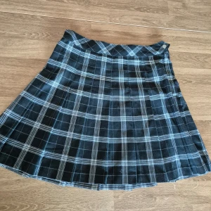 Svart och vit rutig kjol från H&M Divided - Snygg svart och vit rutig kjol från H&M Divided. Kjolen har en klassisk A-linjeform och är perfekt för en stilren look. Den är tillverkad i ett bekvämt material och har en tidlös design. Storlek 38