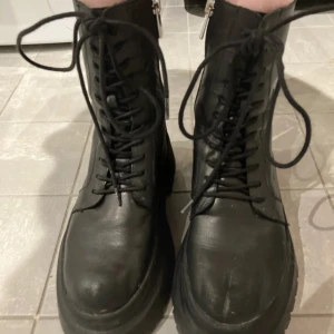 Svarta boots med snörning och dragkedja - Snygga svarta boots i skinn med både snörning och dragkedja för enkel på- och avtagning. De har en robust sula som ger bra grepp och en cool look. Perfekta för att ge din outfit en edgy touch.