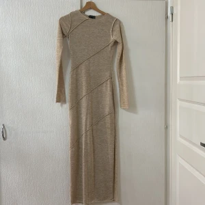 Beige långklänning från PrettyLittleThing - Snygg beige långklänning från PrettyLittleThing med långärmad design. Klänningen har ett diskret diagonalt mönster och är tillverkad i ett mjukt material som ger en bekväm passform. Perfekt för en stilren look.