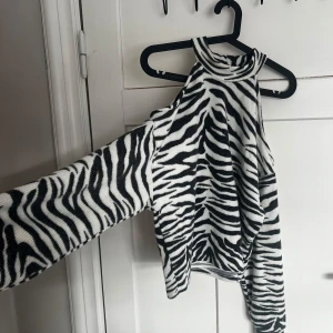 Zebramönstrad stickad tröja - Säljer en trendig zebramönstrad topp med ribbad struktur. Toppen har en unik design med en hög hals och ärmlös stil, perfekt för att sticka ut i mängden. Passar bra till både jeans och kjol för en stilren look.