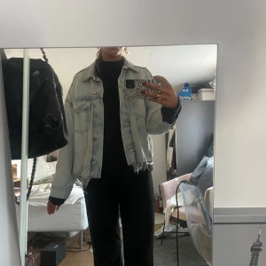 Ljusblå jeansjacka - Säljer en ljusblå jeansjacka med en croppad och fransig nederkant. Jackan har en klassisk design med knappar framtill och två bröstfickor. Perfekt för en avslappnad stil.