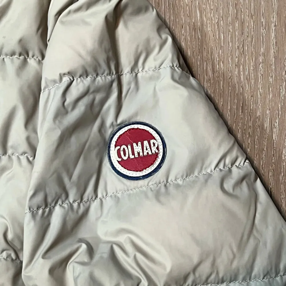 Snygg beige dunjacka från Colmar med huva och dragkedja. Jackan har en quiltad design och två praktiska fickor med dragkedja. Perfekt för kyligare dagar.. Takit.