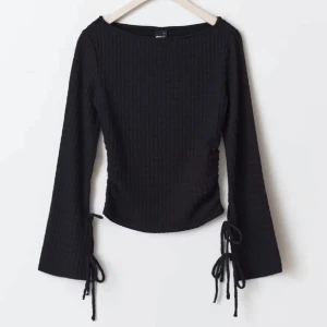 Svart ribbad topp med knytband - Snygg svart ribbad topp med långa ärmar och knytband vid ärmsluten. 