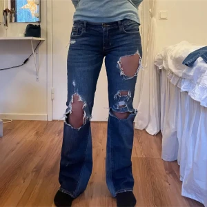 Blå slitna jeans från Abercrombie & Fitch - Säljer ett par blå jeans från Abercrombie & Fitch med slitningar på framsidan och bakfickorna. De har en bootcut-stil, de är utsydda. Innebens längd 74cm. Passar S.  