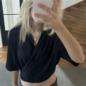 Marinblå omlottopp - Säljer en snygg omlottopp med trekvartsärm. Toppen är croppad och har en stilren design som passar perfekt till både vardag och fest. Den är gjord i ett mjukt och bekvämt material som känns skönt mot huden.