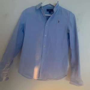 Blå skjorta från Ralph Lauren - Tja säljer en Snygg blå skjorta från Ralph Lauren med klassisk krage och broderad logotyp på bröstet. Skjortan har långa ärmar och knappar framtill. Perfekt för en stilren look till sommaren köpt på nk för 1199 för mer frågor dm mej