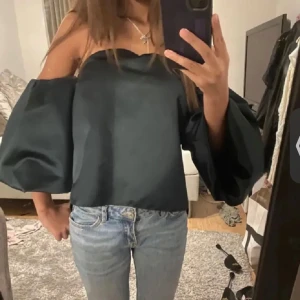 Grön offshoulder blus - Snygg grön offshoulder blus med vida ärmar. Perfekt för en stilren look. Blusen har en elegant och modern design som passar till många tillfällen.