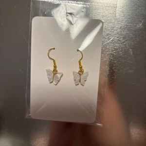 Guldörhängen med fjärilsdetalj - Snygga örhängen med guldfärgade krokar och hängande fjärilar i transparent material. Perfekta för att ge en elegant touch till din outfit. Finns 3 par (Billigt material) 