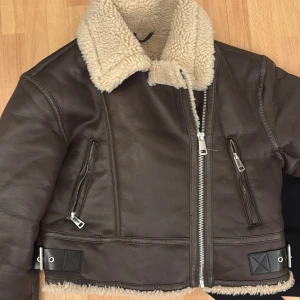 Brun skinnjacka med foder - Snygg brun skinnjacka med mjukt foder och dragkedja framtill. Jackan har en klassisk design med två fickor med dragkedjor och en bred krage. Perfekt för kyligare dagar.