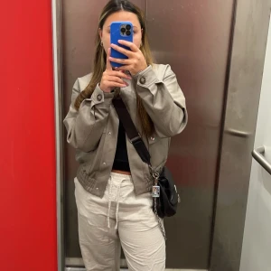 Grå jacka från Vero Moda - Säljer en snygg grå jacka från Vero Moda. Jackan har en kort design med knappar och elastisk midja. Perfekt för en stilren look. HELT NY med prislapp kvar, passar XS/S