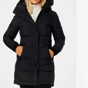 Svart dunjacka med huva - Snygg och varm svart dunjacka med huva och dragkedja. Jackan har långa ärmar och praktiska fickor framtill. Perfekt för kyliga dagar.